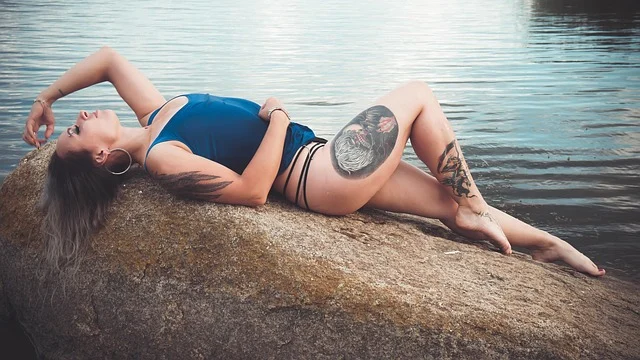Boy shorts for women: A tattooed woman in swimwear reclining on a rock by water
