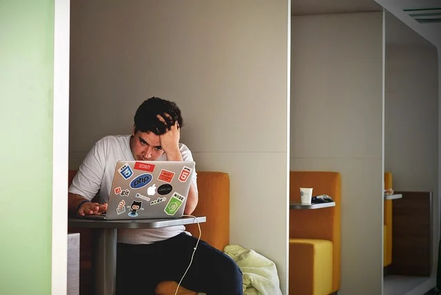 A stressed man holding his head while looking at a laptop
