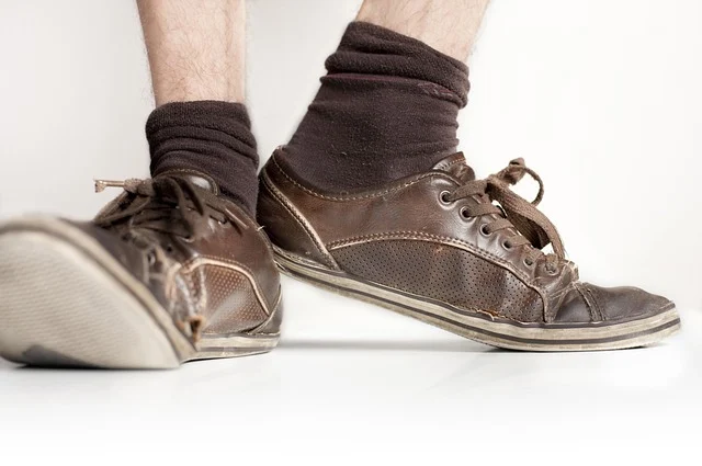 Worn and damaged brown leather sneakers on feet