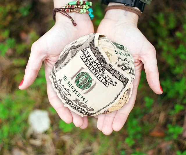 Hands holding a ball made of US dollar bills outdoors