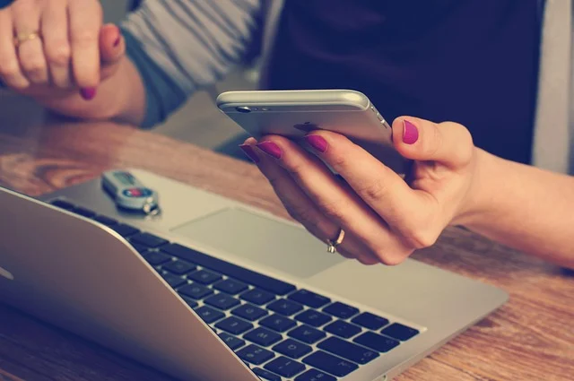 A person holding a smartphone while working at a laptop