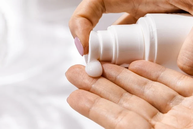 A person dispensing skincare cream onto their hand from a pump bottle