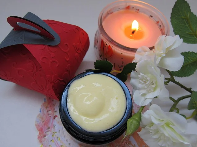 An open jar of cream surrounded by flowers and a candle