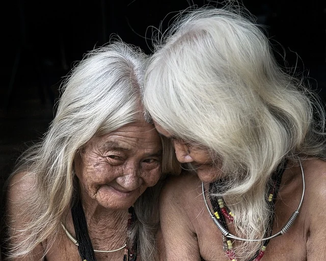 Two elderly women with long grey hair leaning close together
