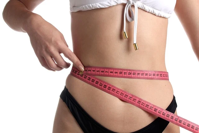 A woman measuring her waist with a pink measuring tape
