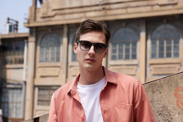 A stylish man wearing sunglasses and a pink shirt outdoors