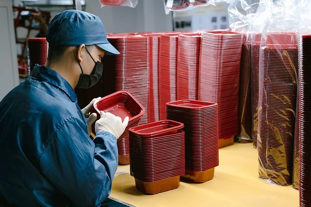 A factory worker inspecting red plastic containers on a production line