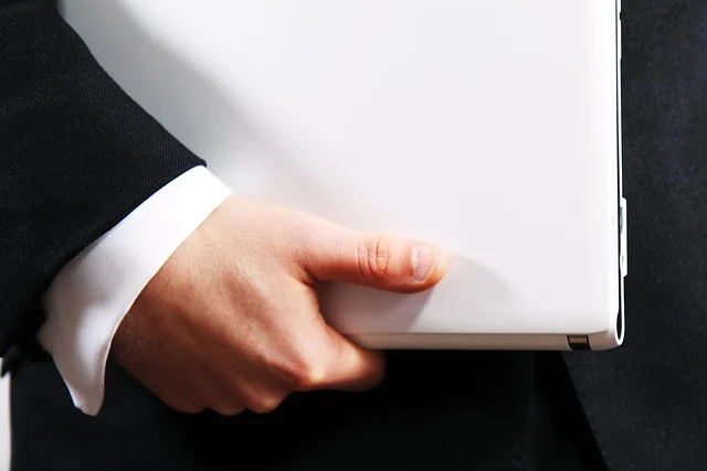 A professional in a suit holding a closed white laptop