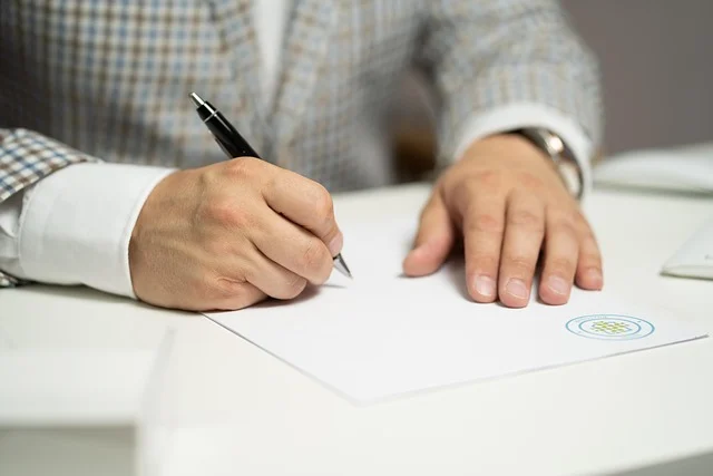 A person in a suit signing a document with a pen