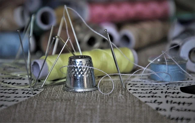 Sewing needles, a metal thimble, and spools of thread