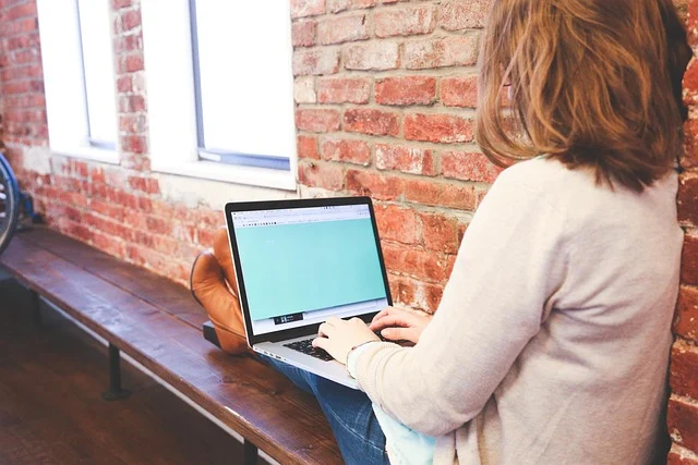 A woman using a laptop to search online near a brick wall
