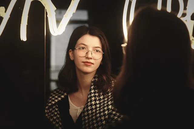 A young woman with glasses wearing a houndstooth pattern in a mirror reflection