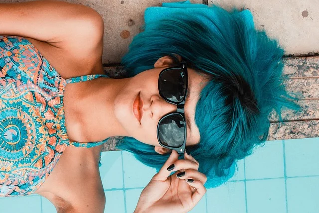 A woman with tanned skin and blue hair lying by a pool