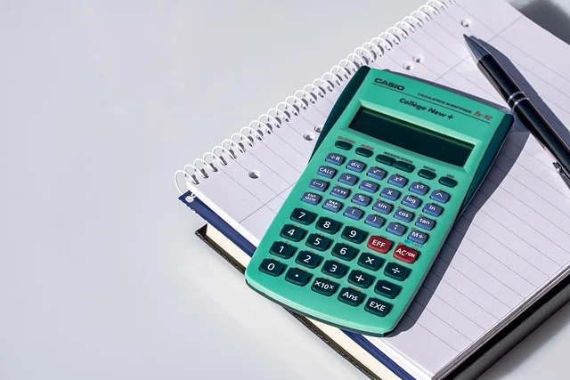 A green calculator resting on a notebook next to a pen