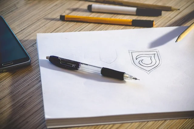 A sketch of a logo emblem on paper with stationery nearby