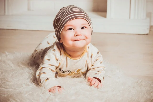 A smiling baby lying down wearing a striped beanie and onesie