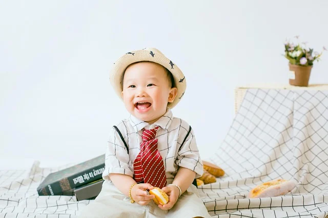A smiling baby boy wearing a hat and a red tie