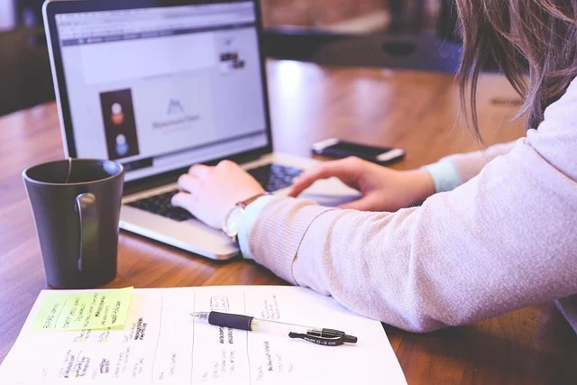 A person typing on a laptop at a desk with paperwork nearby