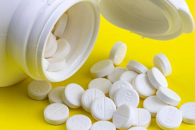 White pills spilling out of a plastic bottle on yellow background