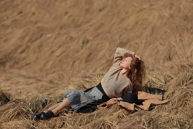 A woman in a mesh sweater and skirt lying on dry grass