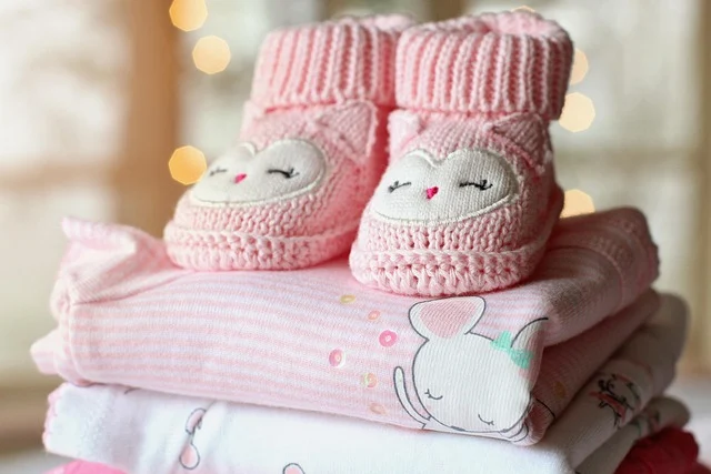 Stacked folded pink baby clothes with knitted booties on top