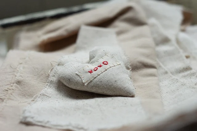 A heart-shaped fabric cushion with XOXO embroidery on linen material