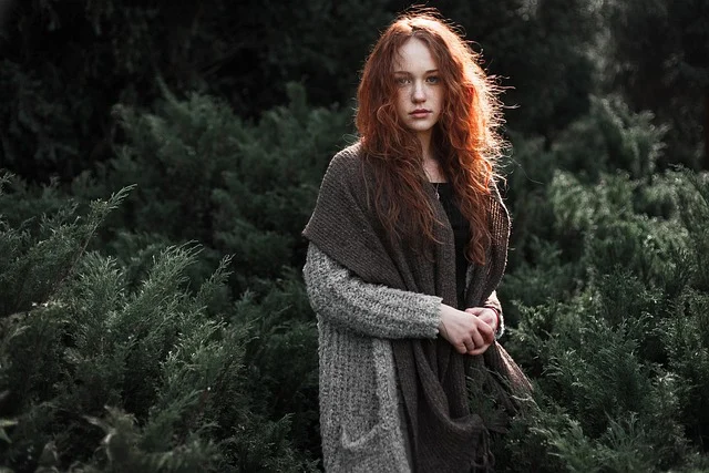 A red-haired woman wearing a cozy cardigan and scarf in nature
