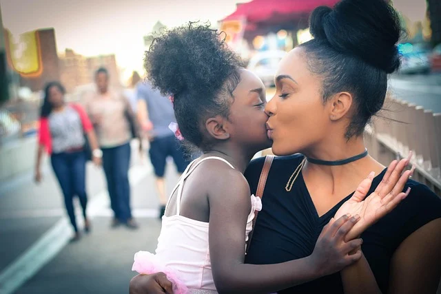 A mother holding and kissing her young daughter outdoors