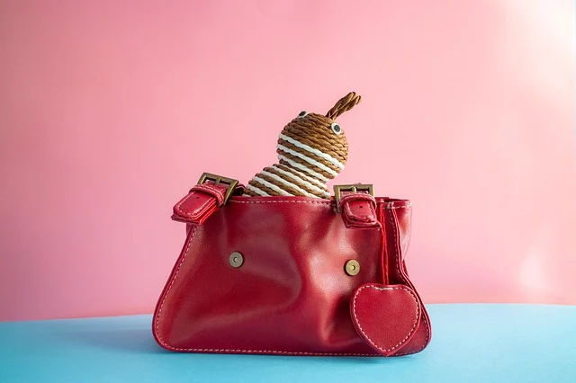 A small red handbag with a woven toy inside on a colorful background