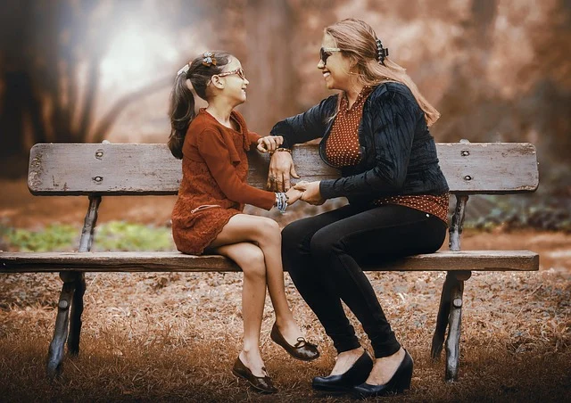 A mother and daughter holding hands while sitting on a park bench