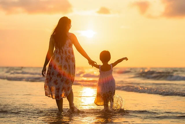 A mother and daughter wearing matching dresses walking on the beach at sunset