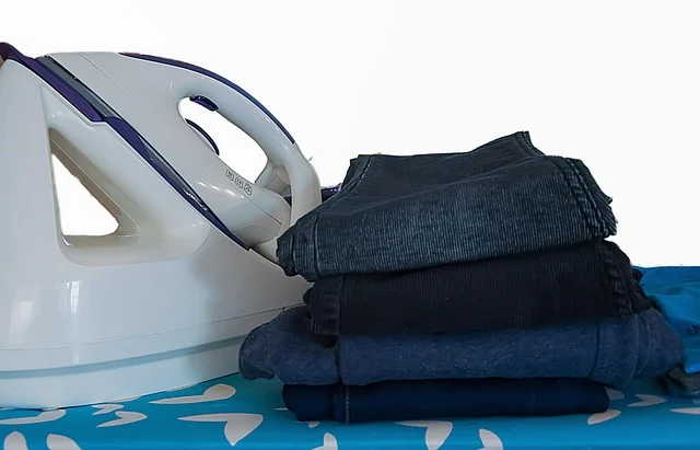 An iron next to a stack of folded trousers on an ironing board