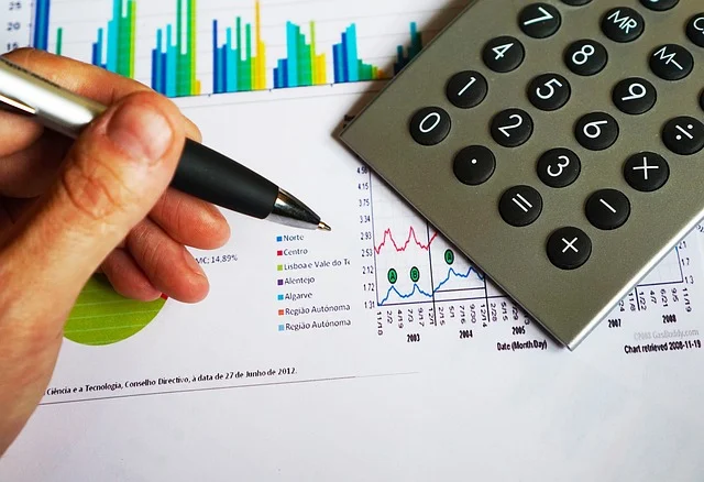 A hand holding a pen over financial charts next to a calculator