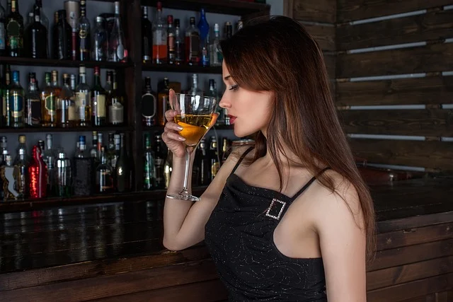 A woman in a black cocktail dress holding a drink at a bar
