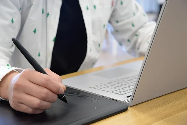A person using a graphics tablet and stylus next to a laptop