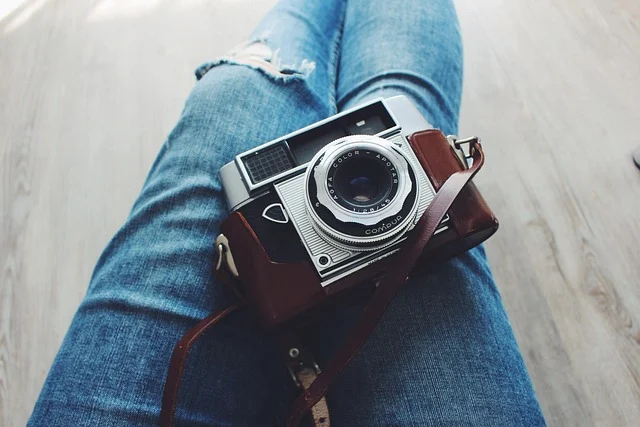 A person wearing ripped jeans holding a vintage camera on their lap