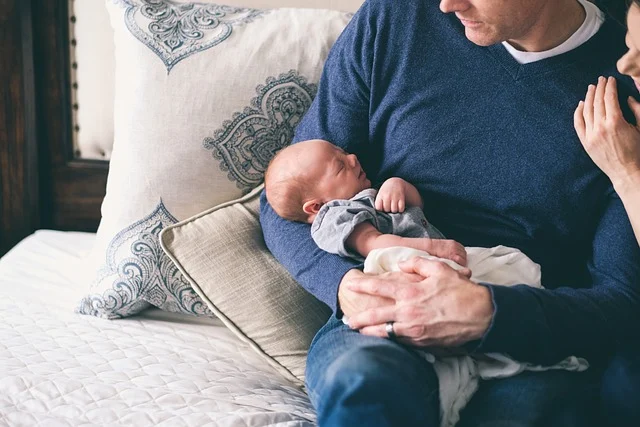 A father holding a sleeping newborn baby with mother nearby
