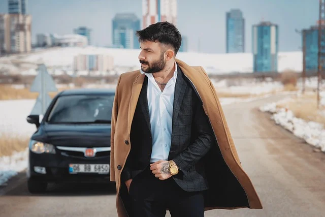 A man wearing a brown overcoat over a suit jacket outdoors