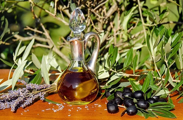 A glass decanter of olive oil with fresh olives and lavender