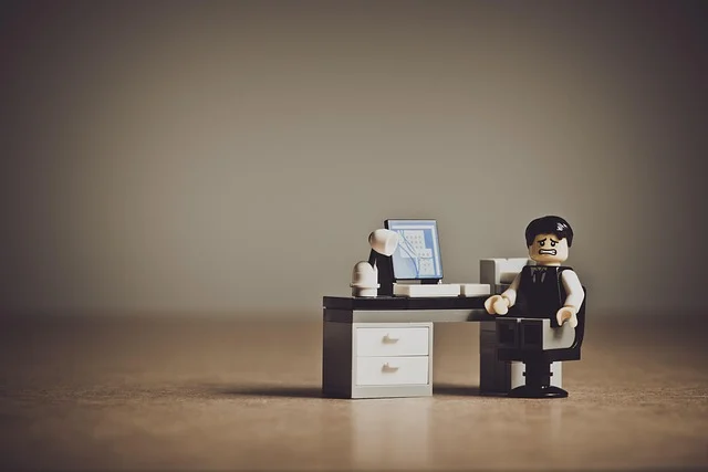 A stressed Lego mini-figure sitting at a desk with a computer