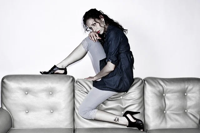 A woman wearing a denim top and leggings posing on a sofa