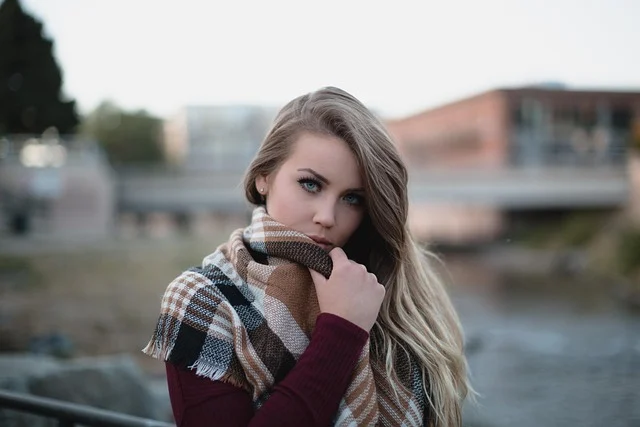 A young woman wearing a plaid scarf and burgundy top outdoors
