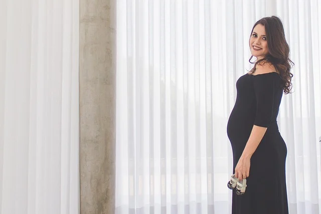 A pregnant woman in a black dress holding baby shoes
