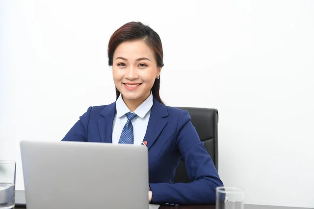 A woman in a formal blue suit sitting at a laptop