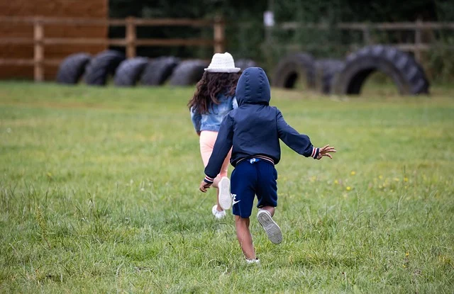 Two young children running through a grassy field