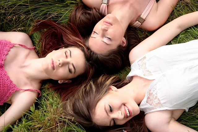 Three young women lying on grass wearing casual summer tops