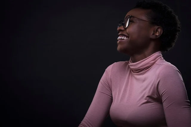 A smiling woman wearing glasses and a pink turtleneck top