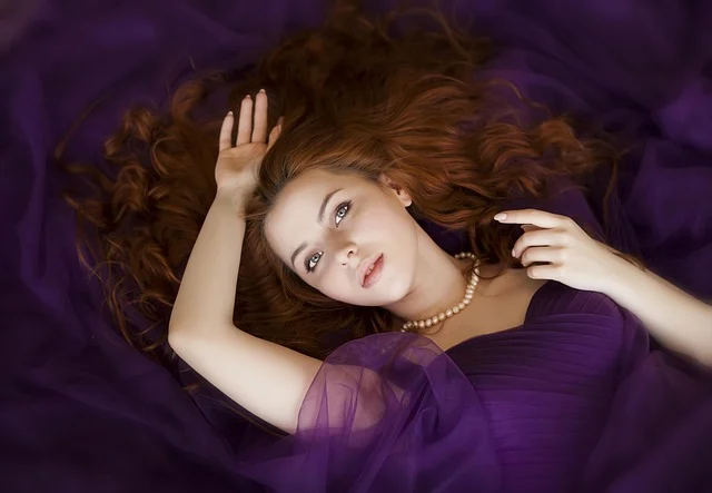 A woman lying in purple fabric wearing a pearl necklace