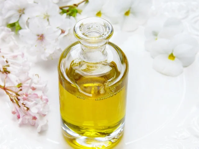 A glass bottle of golden oil surrounded by white flowers