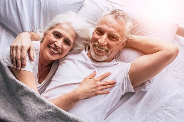 An older couple smiling together while lying in bed